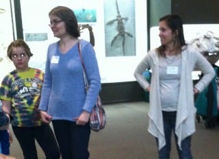 Kate Chritton, 10, of West Hartford (left) joined others in the dinosaur room of the Yale Peabody Museum of Natural History to read the first chapter of The Great Connecticut Caper, a serialized e-book being released through Connecticut Humanities’ website. Chapter 1 was written by West Hartford author Lisa Renfro, Kate’s mom, pictured in the blue sweater. Submitted photo