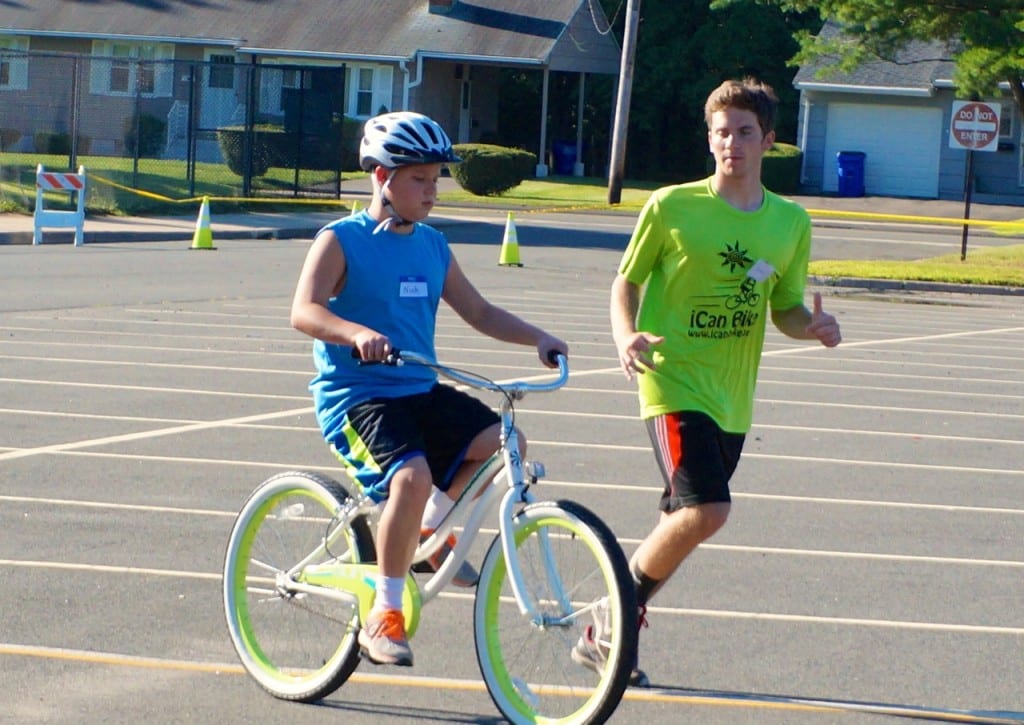 Nick Smith is successfully riding his own two-wheeler without assistance following the iCanBike program. Volunteer Sam Newton runs alongside him. Photo credit: Ronni Newton