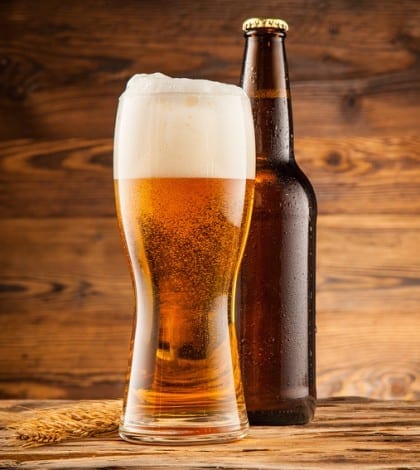 Glass and bottle of beer with wheat ears on wooden planks