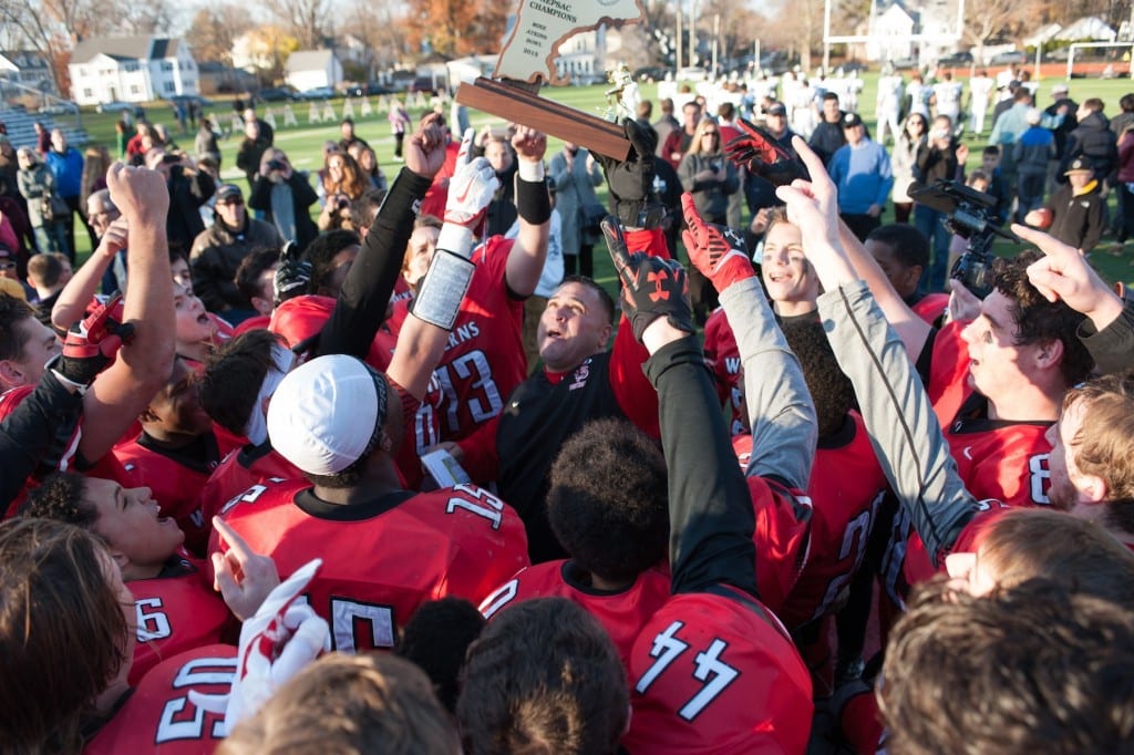 Kingswood Oxford Varsity Football Coach Jason Martinez holds high the Mike Atkins New England Championship Trophy as jubilant Wyverns celebrate their first-ever Bowl win in the school’s 106-year history. Photo credit: Clay Miles