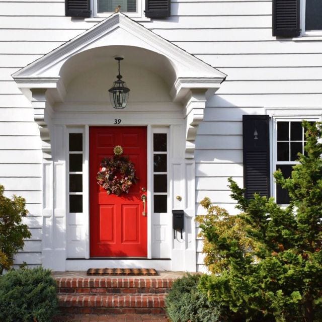 A classic red front door with brass accents and harlequin door mat brightens up this colonial. Photo credit: Deb Cohen