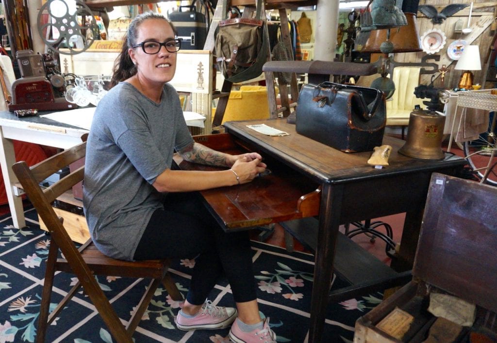 Co-owner Gina Ferrucci sits at one of her favorite items – a hinged desk with a space that once held an inkwell. Old Crow Vintage sells vintage, antique, and repurposed items. Photo credit: Ronni Newton
