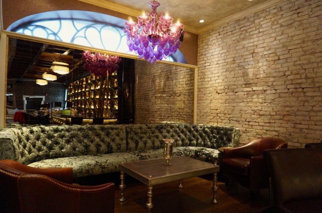 A plush sofa booth lit by a purple chandelier in the front bar area of Noble & Co. in West Hartford. Photo credit: Ronni Newton