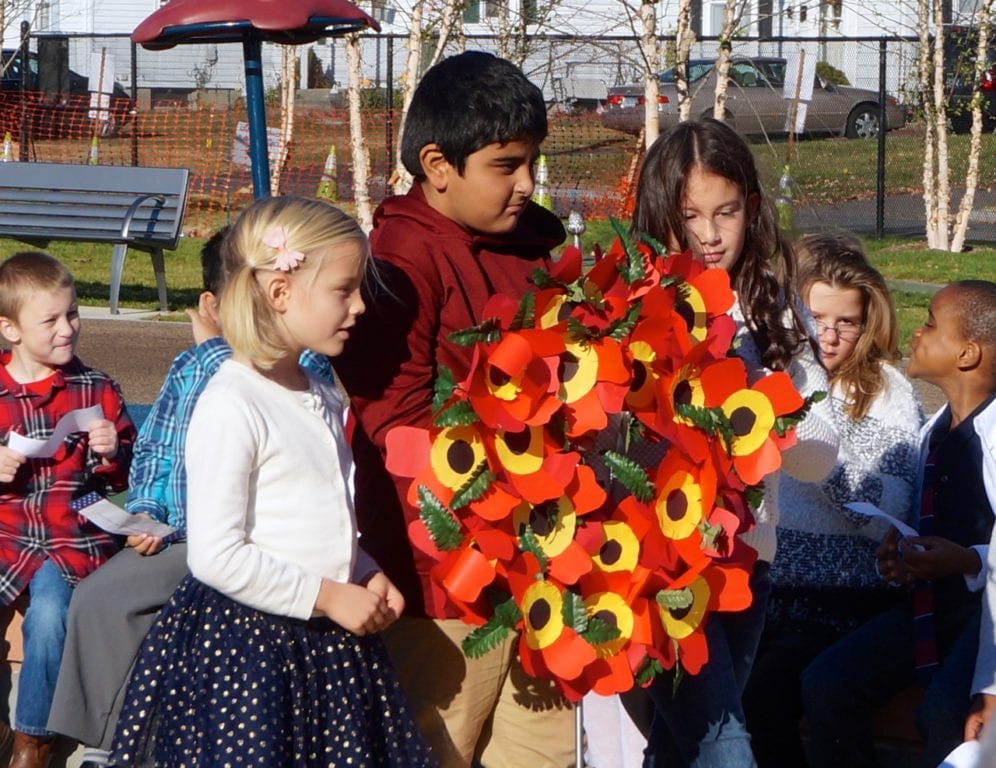 Charter Oak International Academy students (from left) Ruby Hughes, Arnav Kandel, and Arycelli Ruffasto place a wreath honoring veterans at the base of the flagpole. Veterans Day 2016. Photo credit: Ronni Newton