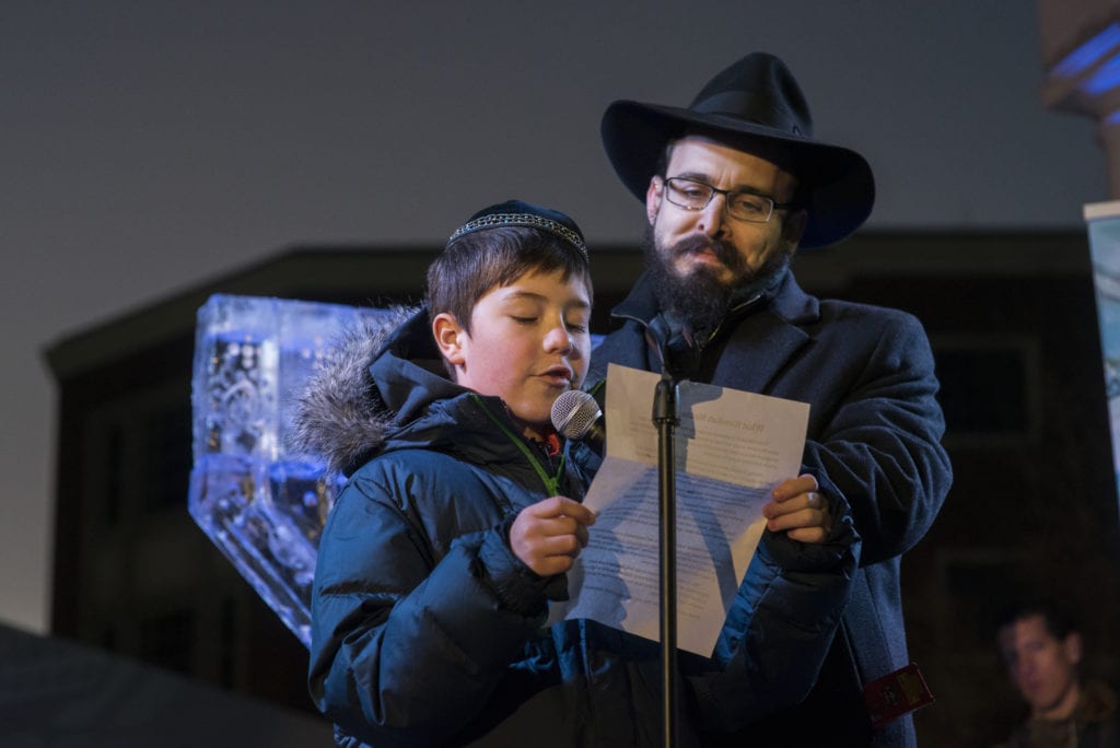 Chanukah Essay winner Mark Kirzon, age 10, reads his winning essay in front of the nearly 1,000 people, before the lighting of the Ice Menorah. At right is Rabbi Shaya Gopin of Chabad. Submitted photo