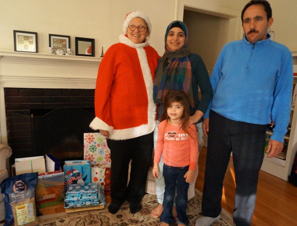 Nancy Latif of Refugee Advocate Services, dressed as Santa, delivers gifts to the Kattoub family in West Hartford. Pictured are (from left) Arabia and Anas Kattoub and their 4-year-old daughter, Jana. Photo credit: Ronni Newton