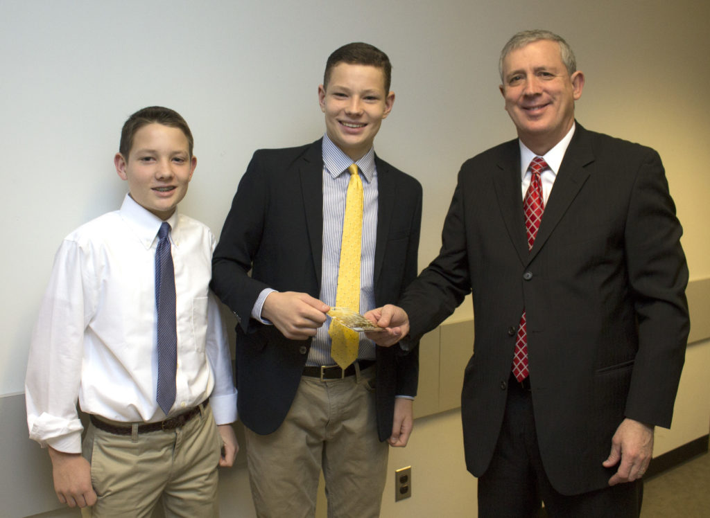 Kenneth Burns, at right, Farmington Bank executive vice president and director of marketing and retail banking, presents a gift to Liam Wilson, center, a West Hartford resident and 9th grade student at Hall High School whose video, Trick Shots to Success, was chosen the winner of the Farmington Bank-sponsored video competition for teenage students about the importance of saving. Wilson’s video has been submitted by Farmington Bank to a national contest called Lights, Camera, Save! organized by the American Bankers Association. Standing at left is Conlan Wilson, brother of Liam, who assisted in the making of Trick Shots to Success. Photo courtesy of Farmington Bank