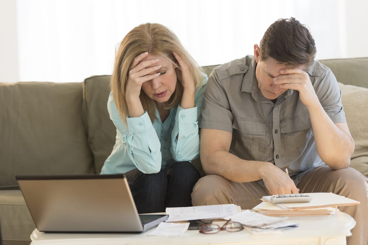 Worried mature couple calculating home finances on sofa